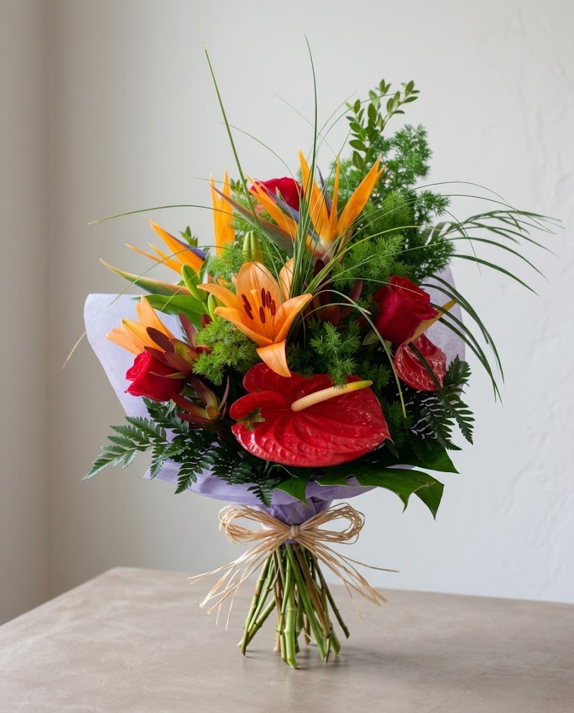Ramo de flores tropicales con lirios naranjas, rosas rojas y follaje verde, envuelto con lazo.