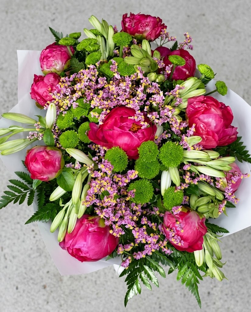 Ramo grande de flores fucsias y verdes con lirios, crisantemos y pequeñas flores moradas sobre fondo gris.