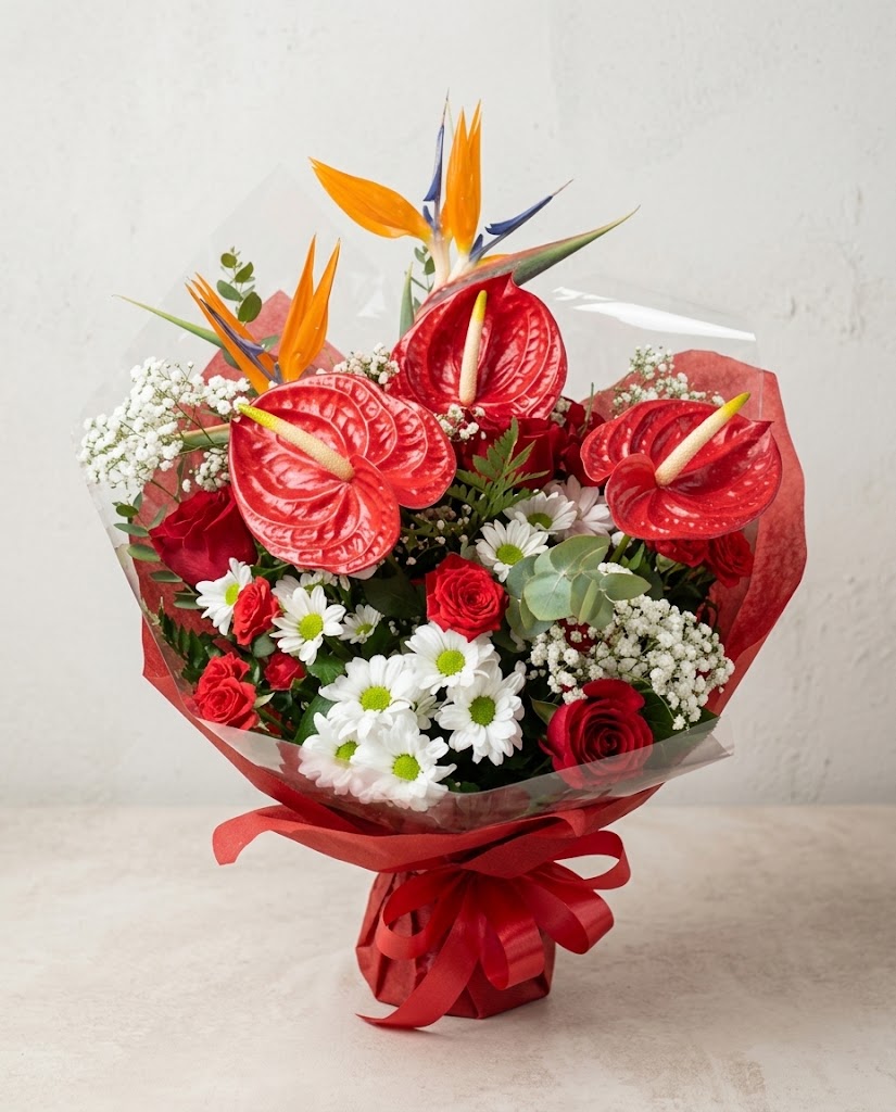 Ramo de flores rojas y blancas con anturios, rosas, margaritas y follaje verde, envuelto en papel.