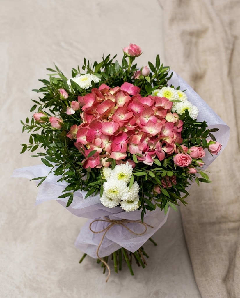 Ramo de flores rosadas y blancas con hortensias, rosas y margaritas, envuelto en papel celeste.