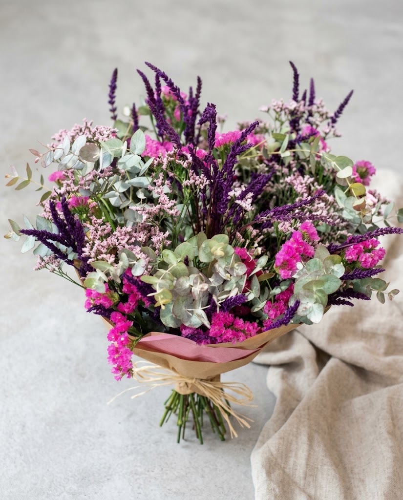 Ramo de flores moradas y rosadas con eucalipto plateado, envuelto en papel kraft y lazo.