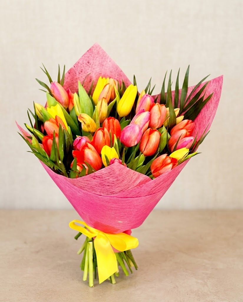 Ramo de tulipanes multicolores envuelto en papel rosa, con lazos amarillos sobre fondo claro..