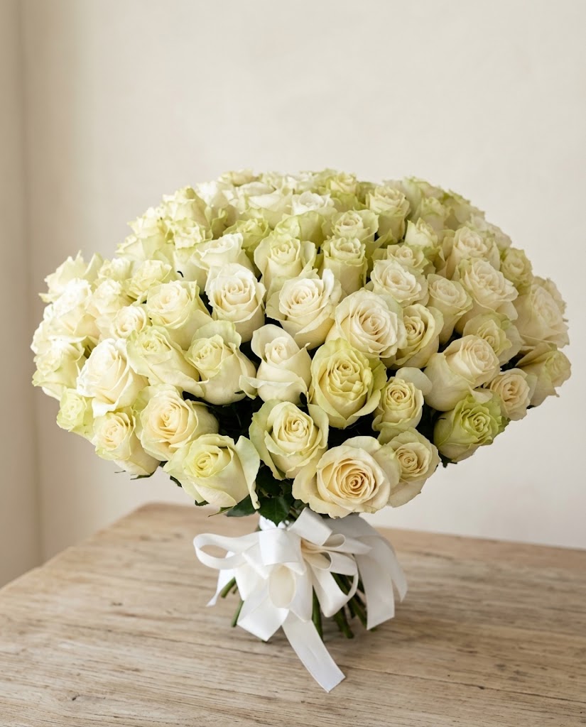 Ramo grande de rosas blancas y crema con lazos blancos sobre mesa de madera clara.