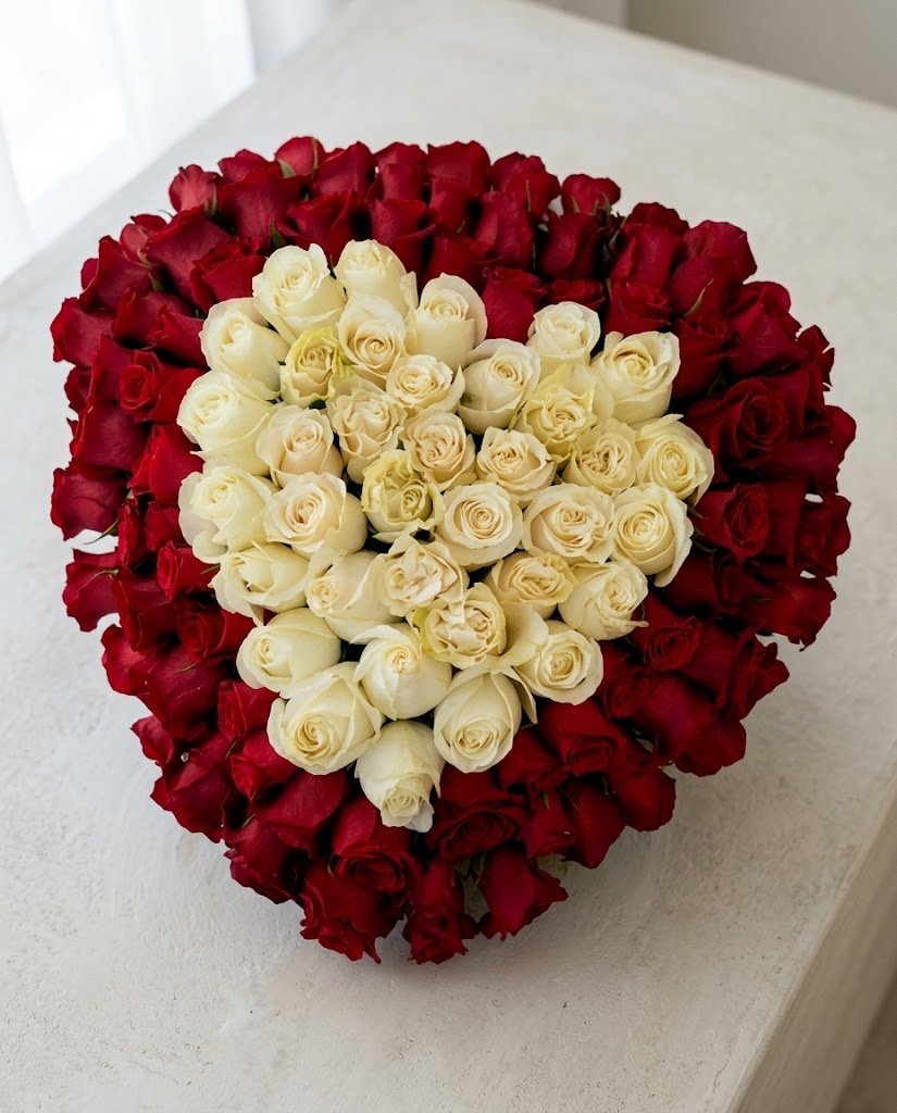 Ramo redondo de rosas rojas y blancas sobre superficie clara, con pétalos densos y fondo luminoso.